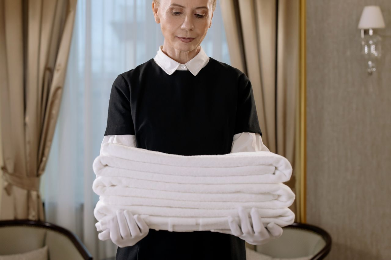 services-01 Professional housekeeper holding a stack of fresh towels in a luxurious hotel room, showcasing elegance and service.